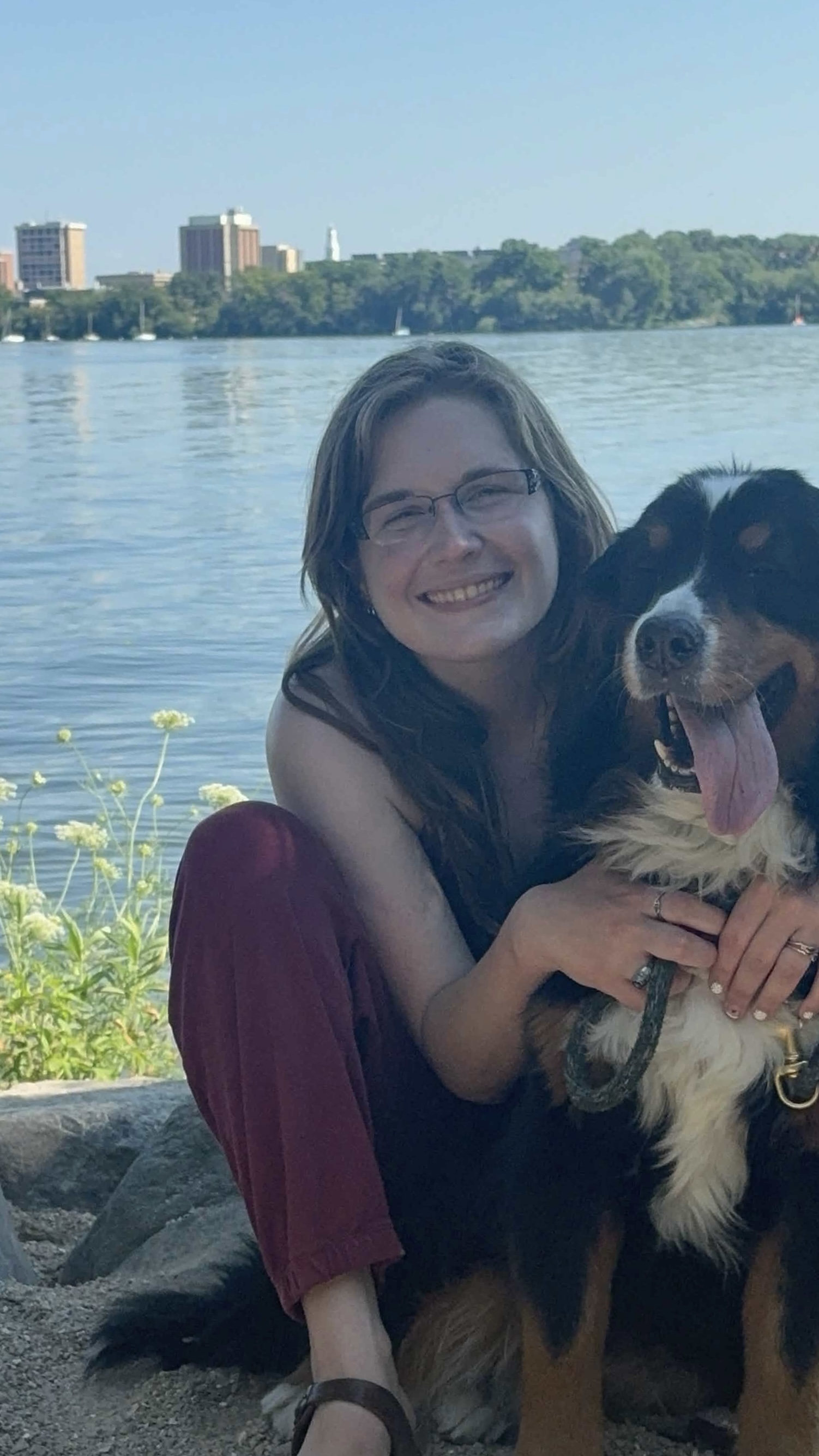 Rachel Turn crouching by the lake beside Chloe, a Bernese mountain dog